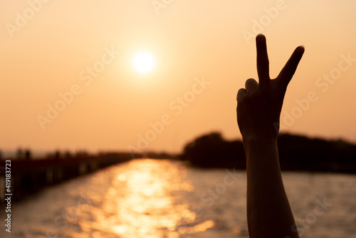 Silhouette of hands holding two fingers on sunset love hope encourage concept, One hand making victory sign at golden hour sunset