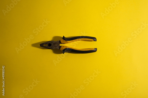 The old yellow-black pliers on the yellow background with traces of dirt