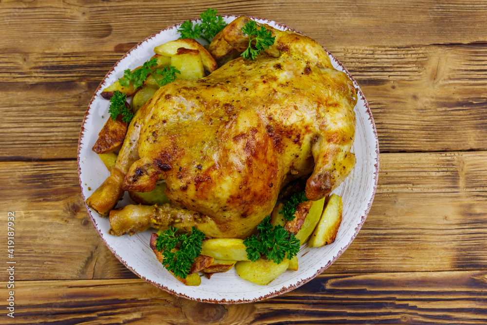 Baked whole chicken with potato on a wooden table. Top view Baked whole chicken with potato on a wooden table. Top view