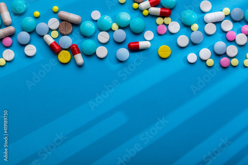 A lot of multi-colored pills on blue background with free space for text, as a concept of medical treatment with a prescription. Painkillers and antibiotics variation, allergy on medicine.