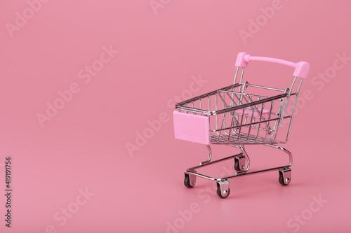 Shopping cart against pink background with copy space. Concept of online shopping and commerce