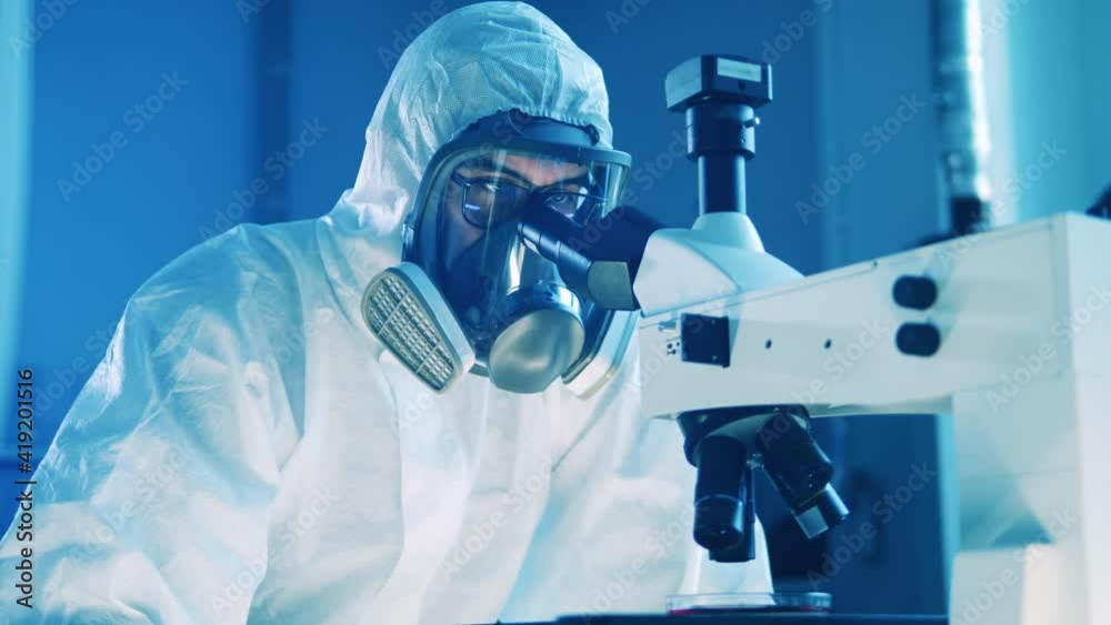Scientist in a splash suit is using a microscope Scientist in a splash suit is using a microscope