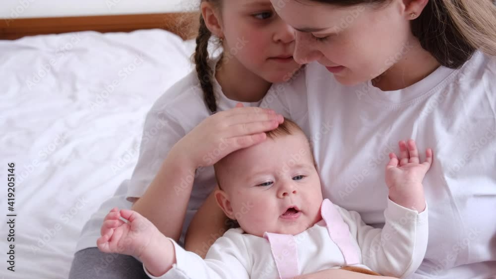 Close up of loving young mom hug cuddle little infant toddler and kiss little daughter, happy caring caucasian mother embrace lull two small girl sister child, enjoy tender moment, childcare concept Close up of loving young mom hug cuddle little infant toddler and kiss little daughter, happy caring caucasian mother embrace lull two small girl sister child, enjoy tender moment, childcare concept