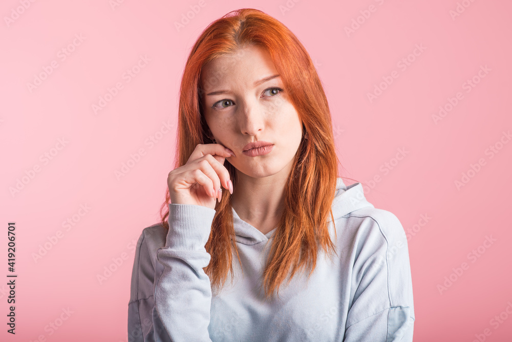 Portrait of a redhead pensive girl in the studio on a pink background Portrait of a redhead pensive girl in the studio on a pink background