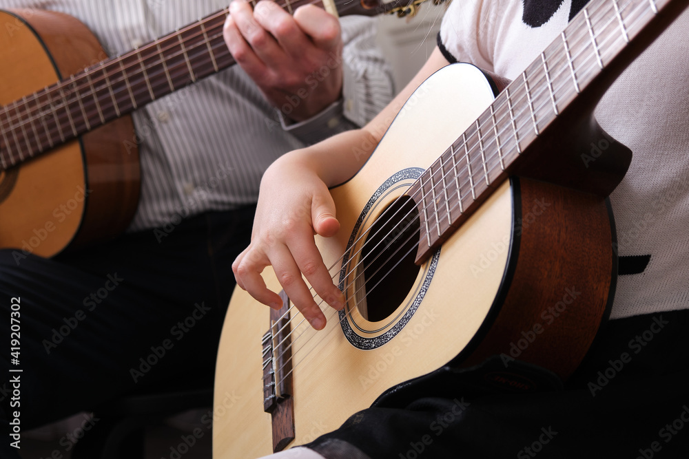 Fototapeta premium little girl and her father are playing guitar. Learning to play the guitar. Music education and extra-curricular lessons.