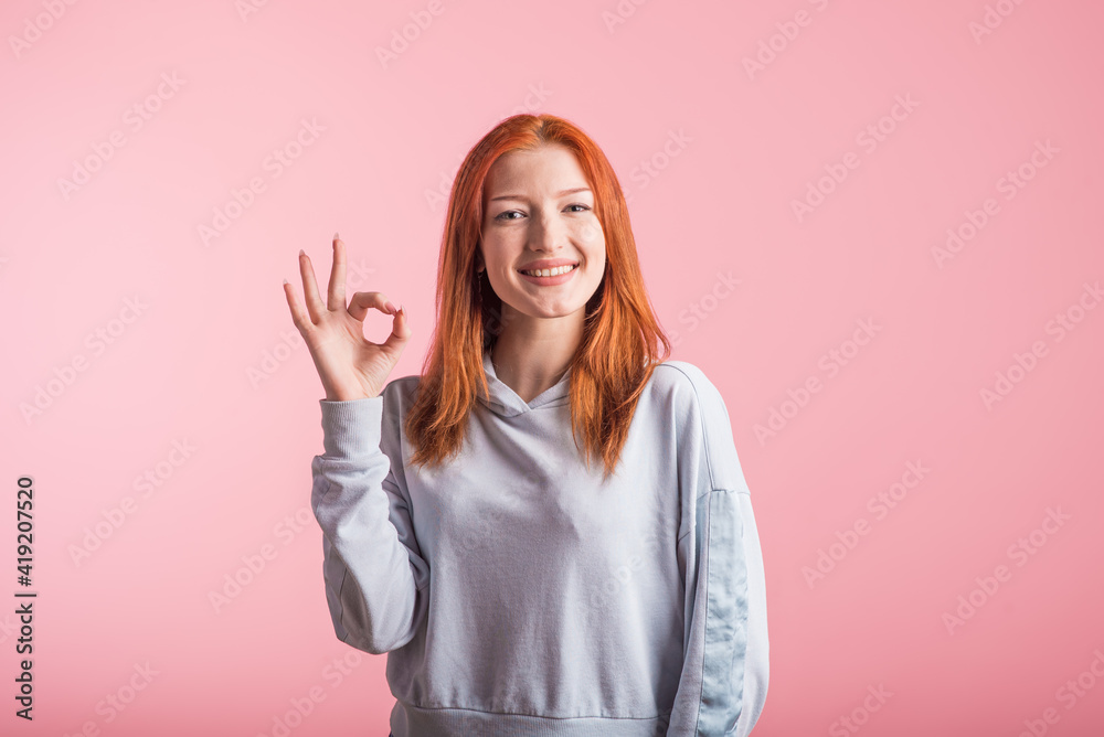 Redhead girl showing Okay gesture in studio on pink background Redhead girl showing Okay gesture in studio on pink background