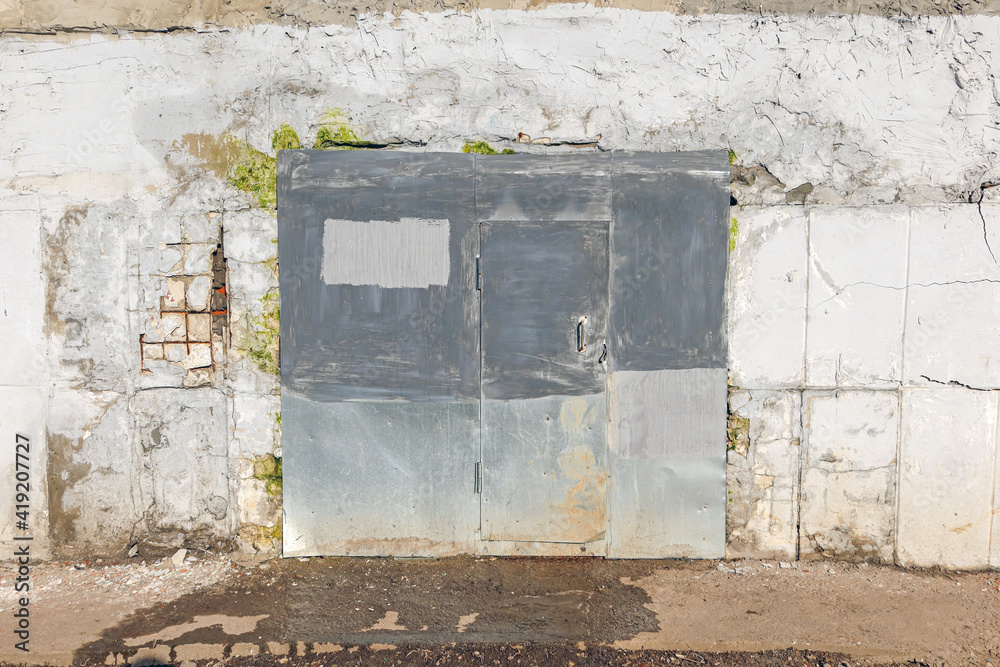 old iron door painted in different colors in a weathered wall with crumbling plaster