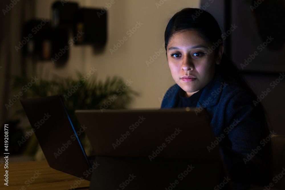 Night shot of a young woman working at home with her computer and tablet Night shot of a young woman working at home with her computer and tablet