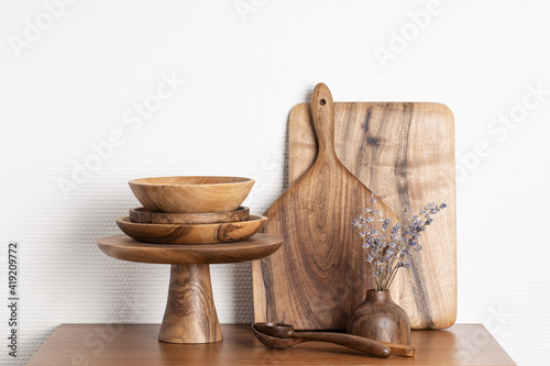 Wooden kitchenware against white wall. Boards, spoons, bowls, cake stand and vase.