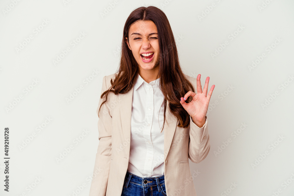 Young Indian business woman isolated on white background winks an eye and holds an okay gesture with hand. Young Indian business woman isolated on white background winks an eye and holds an okay gesture with hand.