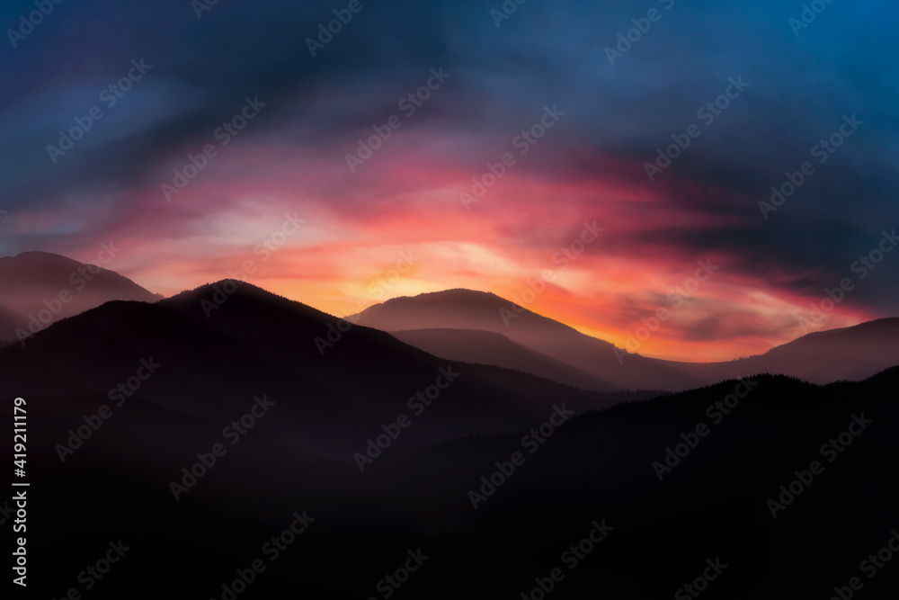 Mountain landscape at sunrise. Dramatic cloudy sunrise sky over mountain tops.