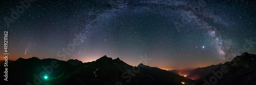 Milky Way arc and stars in night sky over the Alps. Outstanding Comet Neowise glowing at the horizon on the left. Panoramic view, astro photography, stargazing.