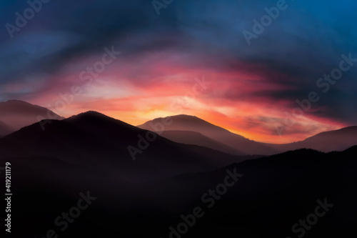 Mountain landscape at sunrise. Dramatic cloudy sunrise sky over mountain tops.