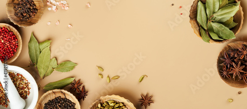 Creative food frame mockup with various types of spices Bay leaf, red chili pepper, anise in wooden bowls on a mocca beige color background with copy space. Long food banner with copy space.