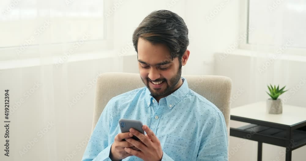 Happy man text messaging using mobile phone at home