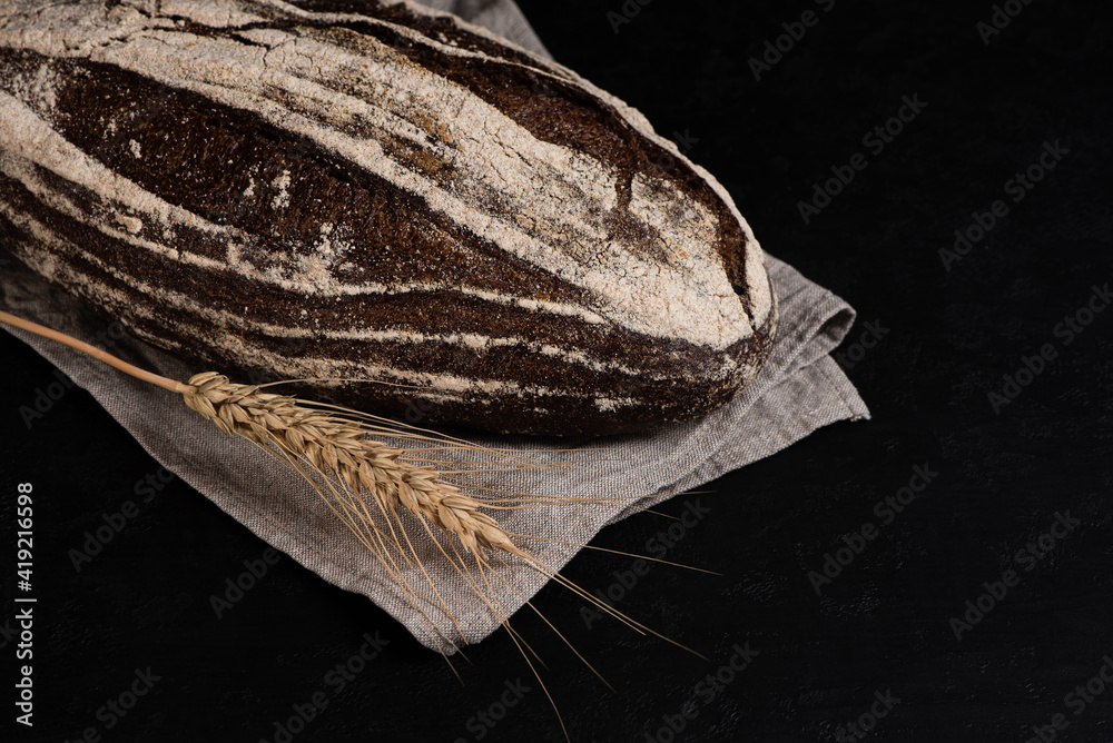 Rustic dark rye bread on black background. Freshly baked sourdough bread. Copy space.