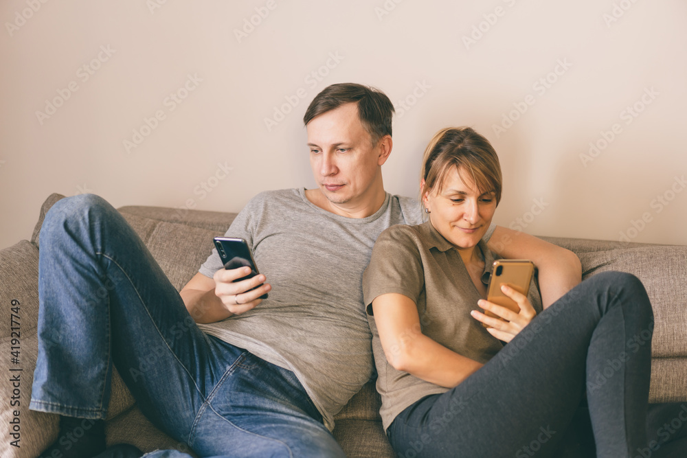 Man and woman sitting on a couch and holding smartphones in their hands. Man and woman sitting on a couch and holding smartphones in their hands.