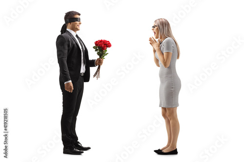 Man in a suit with blindfold giving a bunch of red roses to an excited young woman
