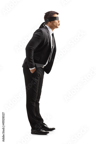 Full length profile shot of a young man in a suit with blindfold blowing a kiss