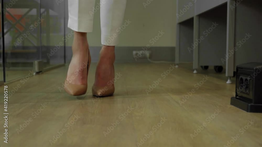 Catwalking beautiful female feet in brown shoes across the office between the rows of desks. Female feet on high heels walking in office in white suit. Young businesswoman walking around the office. Catwalking beautiful female feet in brown shoes across the office between the rows of desks. Female feet on high heels walking in office in white suit. Young businesswoman walking around the office.
