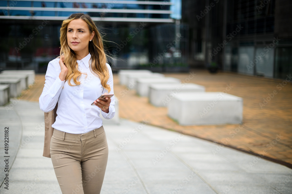 Young female manager walking outdoor while using her smartphone Young female manager walking outdoor while using her smartphone