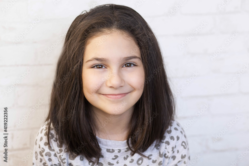 Portrait of a happy smiling latin child girl on white brick wall background