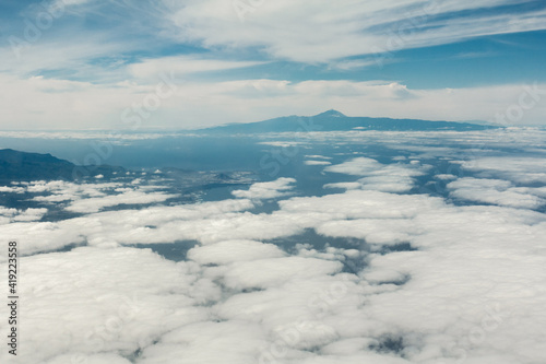  Aerial view of Gran Canaria island and Teide volcano in Tenerife island, Spain. Aerial view from airplane window on blue sky with clouds over a landscape.