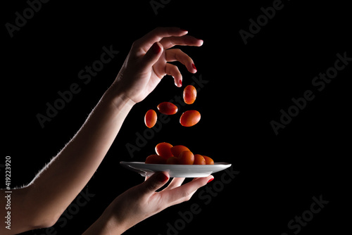 Cherries tomatoes, falling from hands, on a plate with black background and high contrast.Cherries tomatoes on black background.