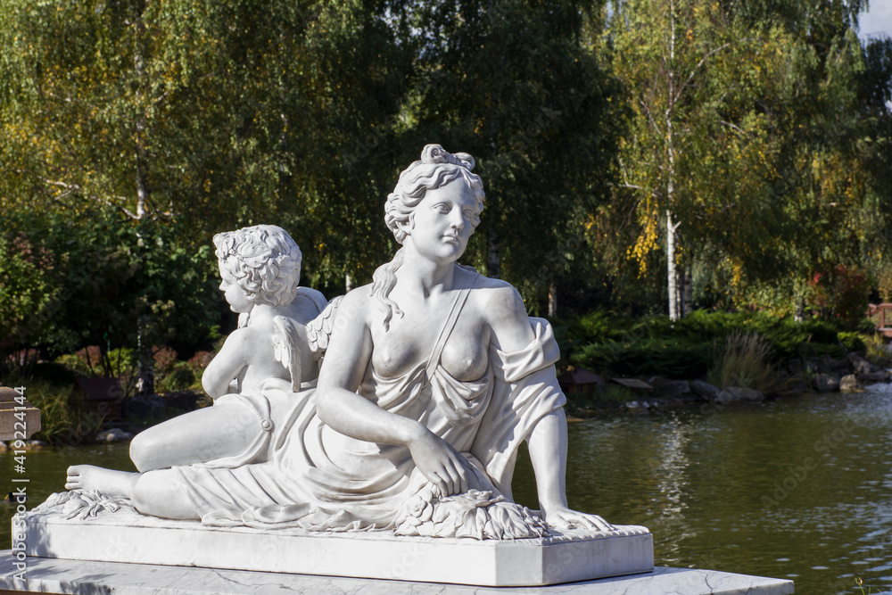 Antique sculpture of the woman Aphrodite and Cupid in the park above the water