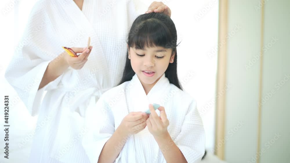 Happy beautiful mom in white bathrobe making her daughter hair at home, Family and Beauty Concept Happy beautiful mom in white bathrobe making her daughter hair at home, Family and Beauty Concept