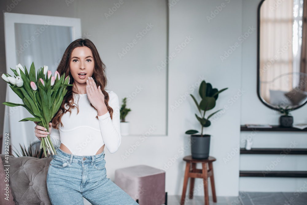 Happy young female smiling and holding bouquet of red tulips while celebrating Women Day