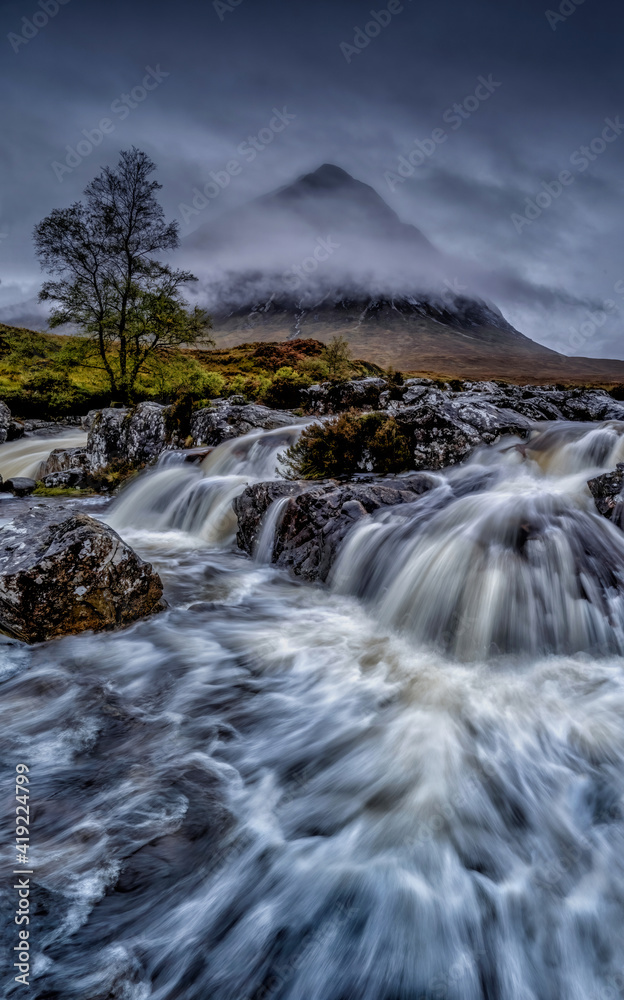 Waterfall in the Scottish highlands near Glencoe, dramatic flowing water against a misty mountain backdrop of Buachaille Etive Mòr