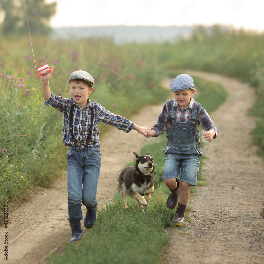Dog and two friends in jeans hats and boots running along the forest road running kite
