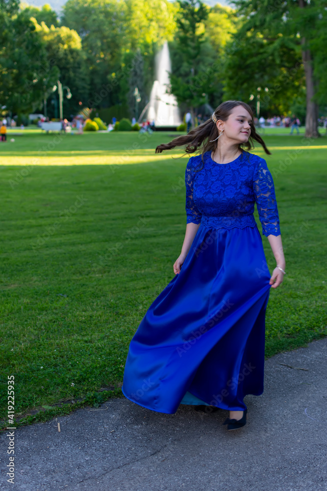 A beautiful graduate girl is spinning in a blue dress in the park