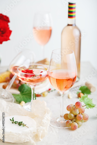 Rose wine in different wineglasses bottle on white table with grapes cheese, snacks bouquet of flowers. modern still life Rose Wine composition on light grey concrete background. Vertical photo