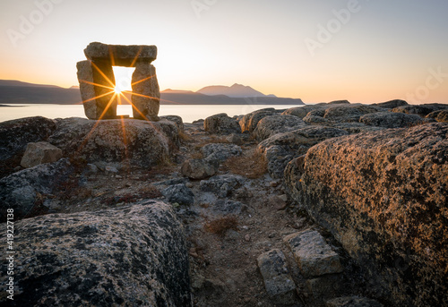 Sunset through Inuksuk in rough arctic landscape. Sunstar on the horizon in the fjord of Qikiqtarjuaq, Broughton Island, Nunavut.