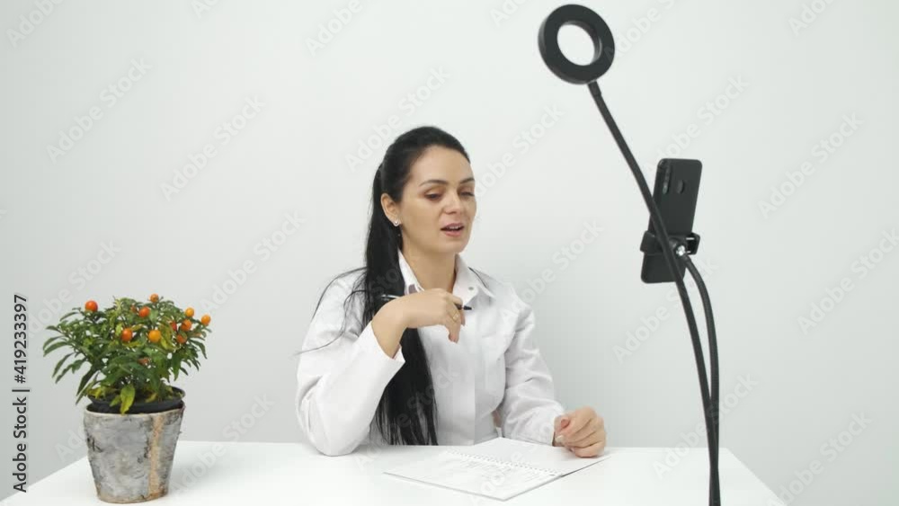 Nutritionist talking on video chat using mobile at work, online consultation. Healthcare professional answering call giving remote consultation on smartphone writing appointment notes. Nutritionist talking on video chat using mobile at work, online consultation. Healthcare professional answering call giving remote consultation on smartphone writing appointment notes.