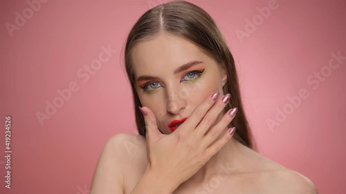 A beautiful model with red lipstick on her lips looks at the camera and with her hand smears the lipstick from her lips, turning beauty into mess make up. FHD footage. 