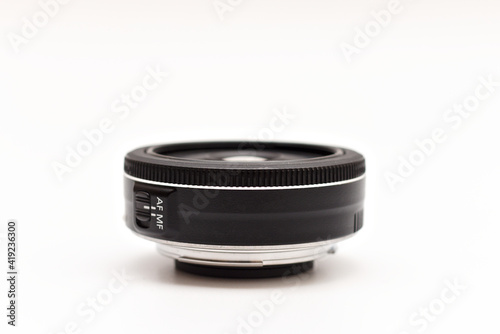 A small thin black 24 mm lens for a dSLR camera without a name lying on a white background without covers. Close-up side view