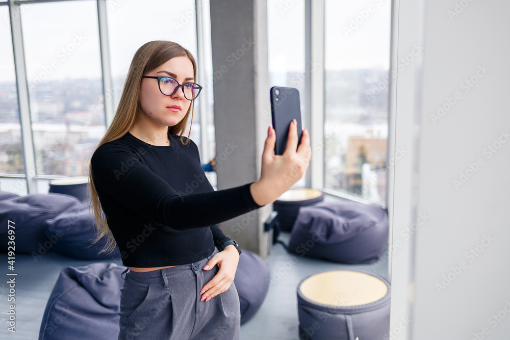 Professional adult businesswoman busy texting on her mobile phone wearing shirt and trousers standing in front of large glass windows. Professional adult businesswoman busy texting on her mobile phone wearing shirt and trousers standing in front of large glass windows.