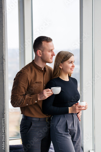 Stylish young couple in love in front of large panoramic windows. Young woman and man stand near a large window