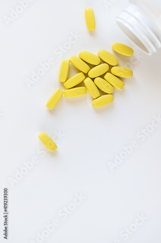Yellow long vitamins lying next to pill jar on white background, macro, close-up, copy space. Nutritional supplements concept, health, vitamins, trendy color of 2021, Illuminating. Vertical