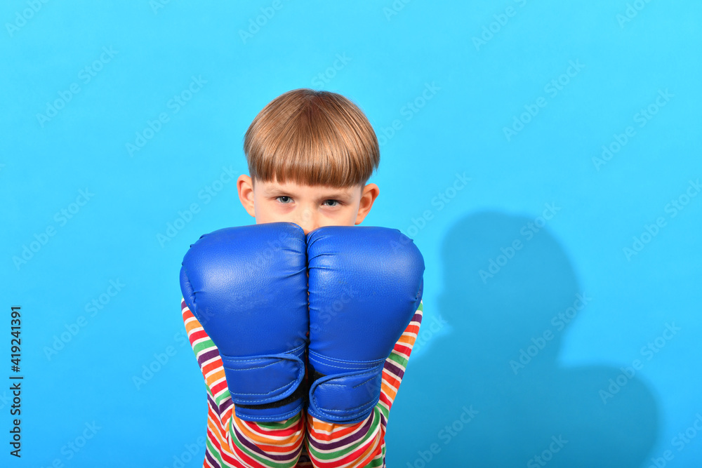 A boy in blue boxing gloves makes a block with his hands in defense against a blow. A boy in blue boxing gloves makes a block with his hands in defense against a blow.