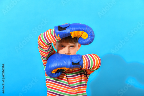 A boy in blue boxing gloves makes a block with his hands in defense against a blow.