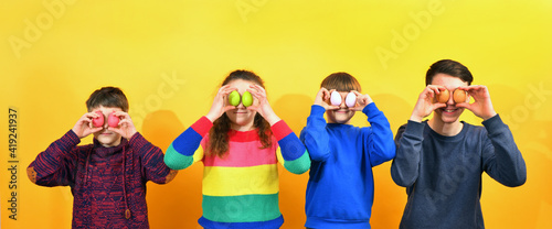 Three boys and a girl hold Easter eggs in front of them on a yellow background.