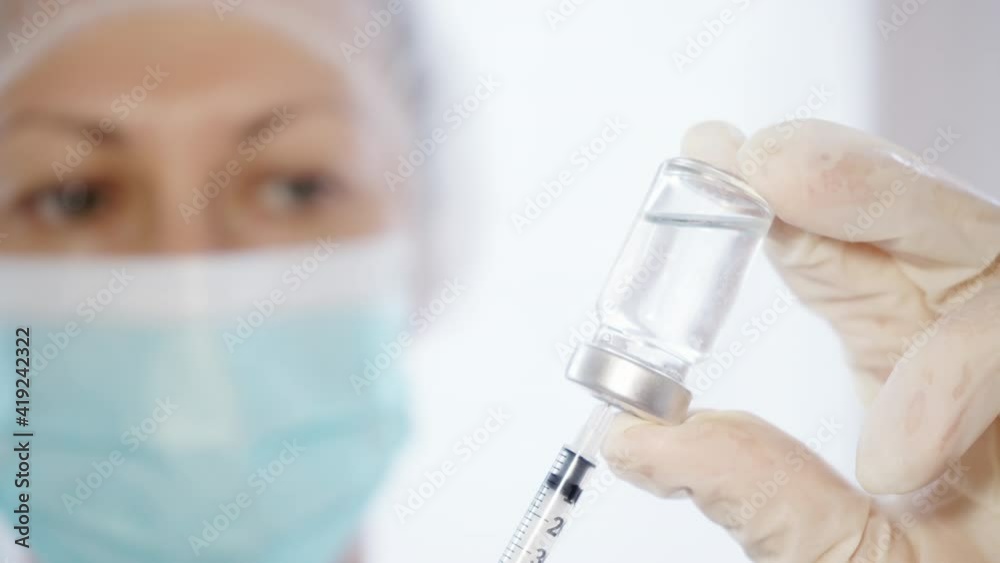 Female Doctor Pouring Medicine Into Syringe. Close-up of Doctor in Medical Mask And Gloves Holding Syringe And Glass Vial Medicine Female Doctor Pouring Medicine Into Syringe. Close-up of Doctor in Medical Mask And Gloves Holding Syringe And Glass Vial Medicine
