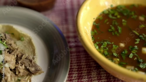 Beef barbacoa taco and bowl of traditional stew on a table