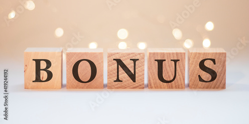 Word bonus cube wood on wooden table white background. Concept bonus is any financial compensation.