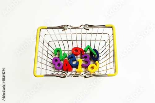 Multicolored wooden numbers in a metal supermarket basket on a white background. Concept: back to school, math, arithmetic, learning to count