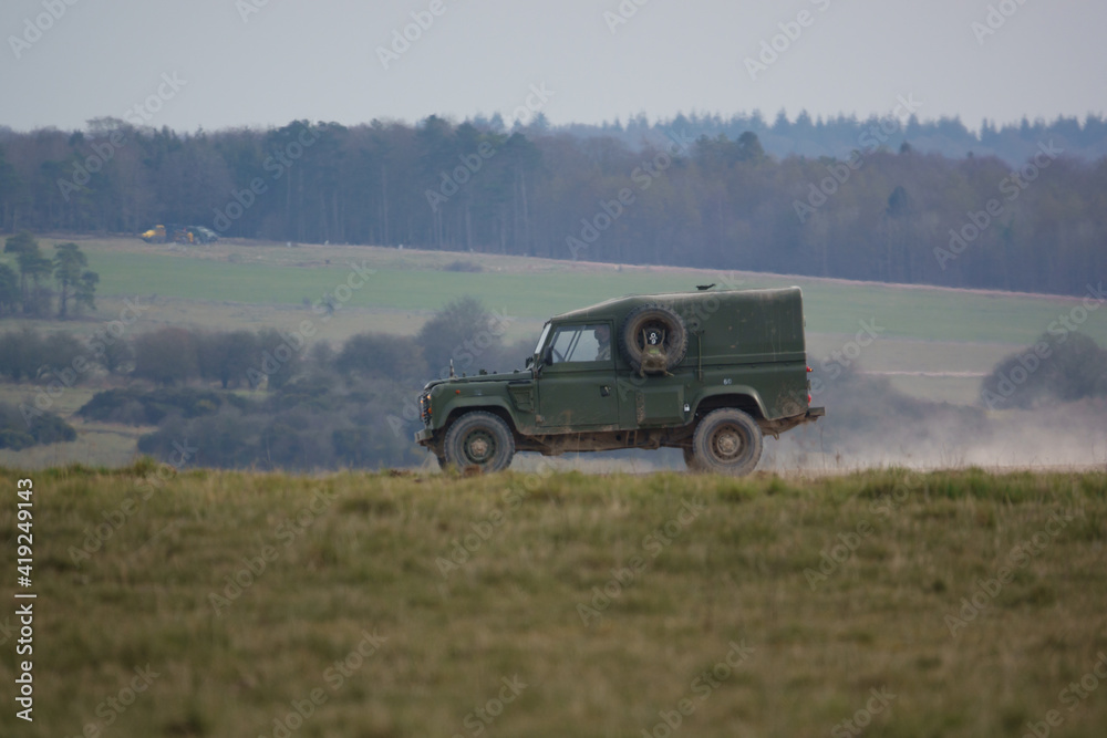 british army land rover defender kicking up dust along a track